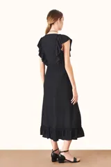 Vestido midi negro con escote en V, corte cruzado, volados en escote y ruedo, y lazo ajustable en la cintura.