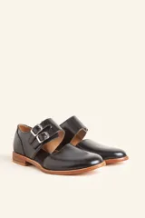 Zapato tipo monk strap con aberturas laterales, confeccionado en cuero vacuno color bordó. Presenta doble tira con hebillas metálicas plateadas en el empeine y suela de cuero con taco bajo.