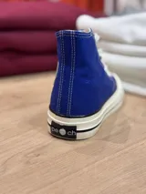 Zapatillas de lona blancas de caña alta con cordones y puntera de goma. Logo de durazno engomado en la base y en la cara interna.