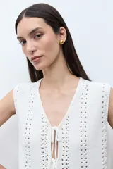 Chaleco sin mangas color blanco crudo, tejido a crochet o punto abierto, con escote en V y cierre frontal mediante lazos cruzados.