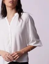 Blusa blanca de gasa marca Sioni, con cuello a la base y escote en V. Tiene abertura central con botones y mangas 3/4 con terminación fruncida.
