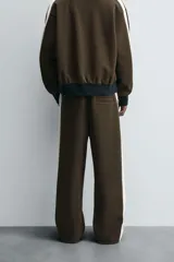 Pantalón jogger color verde oliva, corte relaxed fit, con cintura elástica ajustable con cordón, bolsillos laterales y detalle de bolsillo de vivo en la espalda. Presenta una banda lateral color crema a contraste.
