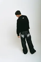 Pantalón de jean negro de corte baggy, con estampado de trigramas blancos en los bolsillos traseros.