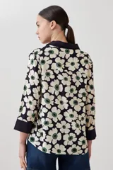 Blusa con estampa de margaritas blancas y verdes sobre fondo azul marino, con cuello polo y mangas 3/4 con puños en contraste.