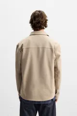 Sobrecamisa negra de tejido con elasticidad, cuello solapa y manga larga acabada en puño con botón a presión. Tiene bolsillos de plastrón en el pecho y cierre frontal con botones a presión.