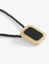 Collar con cordón negro trenzado y dije cuadrado con borde dorado y centro negro.