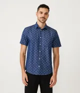 Camisa de manga corta azul con estampado de círculos blancos, cuello camisero, abotonada al frente y con bolsillo en el pecho.