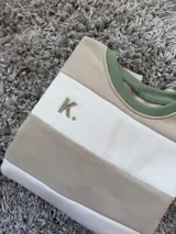 Buzo deportivo a rayas horizontales en color crudo y beige con cuello verde y logo bordado con la letra K.