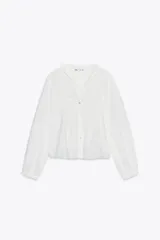 Camisa blanca de cuello alto y manga larga, con detalle de entredós combinados a tono y cierre frontal con botones.