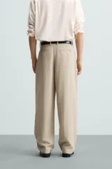 Pantalón de corte holgado (wide fit) en color beige, confeccionado en tejido con mezcla de lyocell. Presenta pliegues frontales en la cintura, bolsillos laterales y bolsillos traseros de doble vivo. Cuenta con cierre frontal de cremallera y botón.