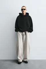 Sudadera negra de tejido con textura acanalada, corte boxy, capucha con cordón ajustable, manga larga con puños acanalados y bajo con elástico.