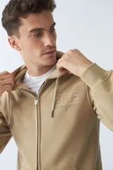 Campera de felpa color beige con cierre frontal, capucha con cordón ajustable, bolsillos laterales y logo estampado en el pecho.