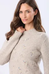 Buzo tejido de abrigo color beige, con cuello redondo y mangas largas. Presenta un delicado diseño bordado en el frente con pequeños motivos en tonos pastel.