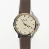 Reloj de pulsera con correa de cuero marrón y esfera redonda color crema con números arábigos y agujas doradas.
