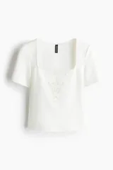 Top corto blanco de punto suave con escote cuadrado amplio, mangas cortas, ajuste entallado y detalle en V de broderie en el centro del busto.