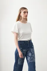 Remera de tejido acanalado color blanco, con cuello redondo y mangas cortas que presentan un detalle de terminación en puntilla en los bordes.