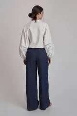 Camisa blanca de mangas largas abullonadas con detalles de calado en los puños, cuello mao y cierre frontal con botones.