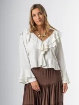 Blusa color crudo en lino rayón con volados, de mangas largas acampanadas y cierre frontal con botones.