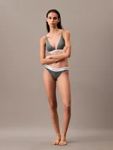 Conjunto Calvin Klein Modern Cotton color verde grisáceo, compuesto por un corpiño triangular con breteles finos y una bombacha clásica tipo tanga. Ambos con cintura elástica blanca con logo de la marca.
