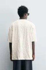 Camiseta color crema de corte holgado, confeccionada en tejido con textura arrugada y cuello redondo.
