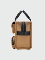 Bolso tote mediano de lona color beige con detalles en negro. Tiene doble asa de mano de cuero y correa bandolera ajustable y extraíble. Cuenta con dos bolsillos frontales con solapa y un bolsillo frontal con cierre. Estampado frontal con la leyenda "THE TOTE BAG" y el logo "MARC JACOBS".
