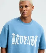Remera masculina de algodón color azul, con corte boxy, cuello redondo y mangas cortas. Presenta una estampa frontal con la palabra "Revenge" en tipografía gótica.