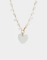 Collar largo con cadena dorada, detalles de piedras blancas irregulares y dije de corazón de nácar.