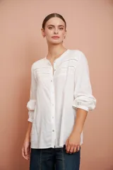 Camisa blanca de manga larga con escote redondo, puntillas y tablas al frente.