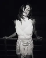 Mini vestido blanco ajustado al cuerpo, con cuello alto y mangas cortas. El diseño se caracteriza por múltiples tiras de tela que se envuelven y anudan alrededor del torso y la cintura.