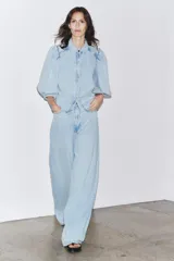 Blusa de denim celeste con cuello solapa y mangas abullonadas por debajo del codo. Cierre frontal con botones.