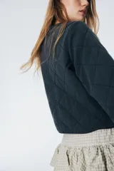 Campera corta acolchada color gris oscuro con cuello redondo, cierre frontal con cremallera y bolsillos laterales. Diseño con patrón de rombos. Forrada.