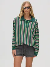 Chomba de corte oversize con cuello camisero, a rayas verticales en color marrón, lila y blanco. Tiene un logo bordado en el pecho y puños en color marrón.