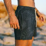 Short de baño negro con estampado de hojas de palmera en blanco. Tiene elástico en la cintura, cordón ajustable, tres bolsillos y mesh interior hipoalergénico.