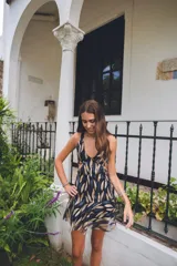 Vestido corto negro con estampado de hojas doradas, escote en V, breteles finos cruzados en la espalda, cut-outs laterales bajo el busto y volado en el ruedo.