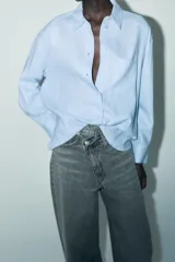 Camisa amplia color negro confeccionada con hilatura de lino. Tiene cuello solapa, manga larga, bolsillo de plastrón en el delantero, bajo asimétrico y cierre frontal con botones.