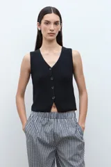 Chaleco de punto color beige melange, con escote en V y cierre frontal de dos botones oscuros. Es sin mangas y de corte ajustado.