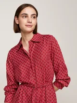 Vestido camisero midi rojo con estampado geométrico blanco, cuello camisero, manga larga con puños abotonados, cinturón anudable y abertura frontal.