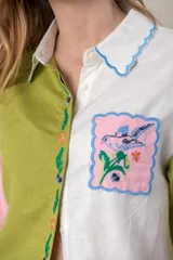 Camisa de mangas cortas con diseño color block en verde, blanco y rosa. Tiene un bolsillo con bordado de ave y flores bordadas en el frente.