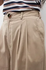 Pantalón de mujer color beige, tiro alto, con pliegues (pinzas) frontales y corte ancho y recto en las piernas.