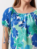 Blusa de seda fría con estampado floral en tonos azules y verdes. Cuello redondo con frunce y mangas cortas amplias con terminación fruncida.