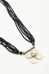 Collar de múltiples cadenas de mostacillas negras con un dije central floral en metal labrado.