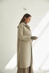 Tapado largo con cuello solapa y corte recto, color gris claro. Tiene cierre frontal con botones ocultos, tajos laterales y bolsillos escondidos en el corte lateral. Está forrado y confeccionado en lana fina sin teñir, diseñada exclusivamente por Don Baez. Hecho 100% en Uruguay.