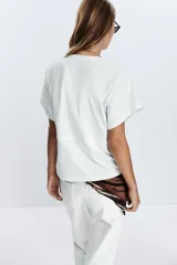 Camiseta color crudo de algodón con cuello redondo, manga corta caída y cintura ajustable con cordón.