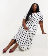 Vestido midi blanco con lunares negros, de corte suelto, cuello redondo y mangas cortas.