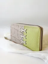 Billetera pequeña de cuero con cierre metálico, diseño color block en verde lima y beige con detalle de cordones cruzados.