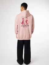 Buzo con capucha color rosa con estampado en la espalda de dos personas llevando una tabla de surf y texto en rojo.