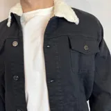 Chaqueta de franela a cuadros en tonos marrón, blanco, azul y naranja, con cuello de corderito blanco, cierre con botones a presión, bolsillos en el pecho con solapa y bolsillos laterales.