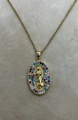 Collar con cadena de eslabones dorados y un dije ovalado con la figura de la Virgen de Guadalupe en relieve. El dije está enmarcado por dos hileras de circonias engastadas en colores variados (blanco, azul, turquesa, fucsia, morado).