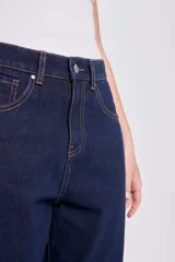 Pantalón de jean azul oscuro, de corte recto y holgado, con el bajo doblado mostrando un forro color bordó.