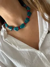 Collar compuesto por cuentas grandes de resina turquesa con veteado blanco y cuentas pequeñas de resina roja, unidos por una cadena ajustable de acero inoxidable.